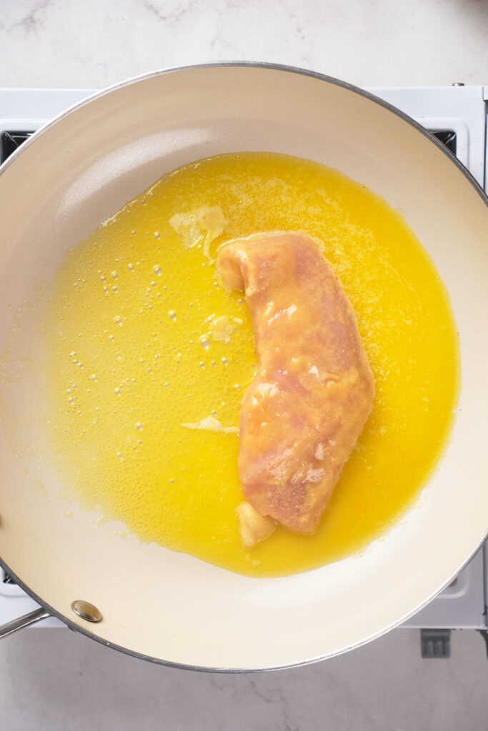 Chicken fillet being shallow fried in a skillet with melted butter.