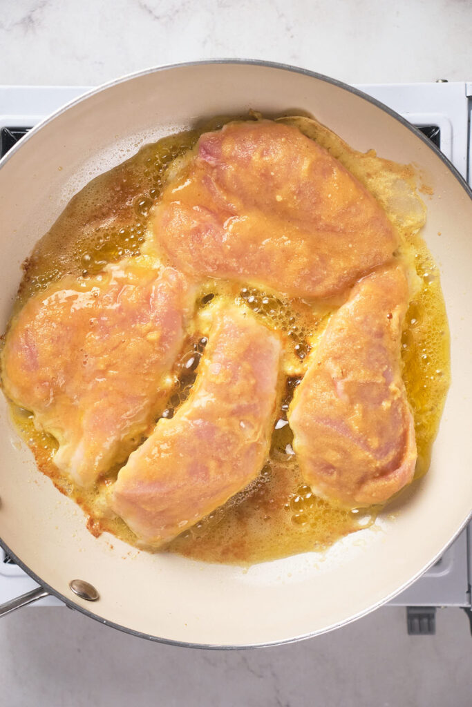 Chicken breasts cooking in a frying pan with oil.