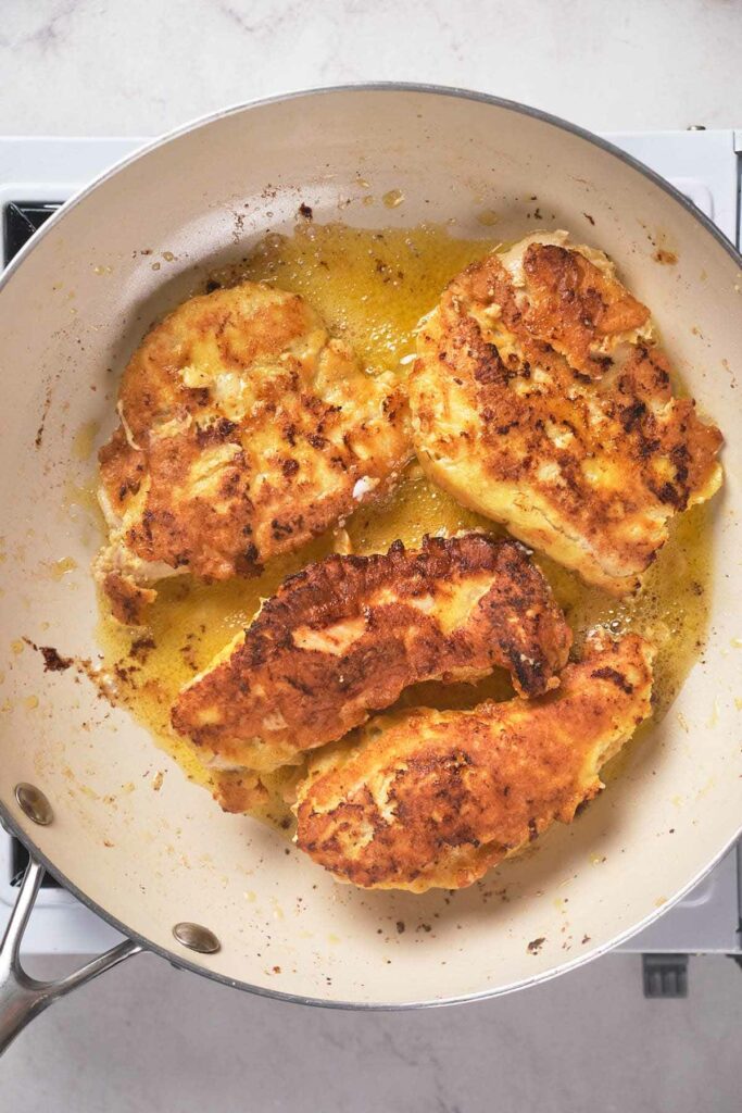 Four pieces of breaded chicken frying in a pan.