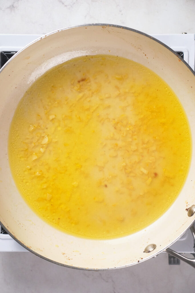 A large white skillet on a stove with butter and garlic.