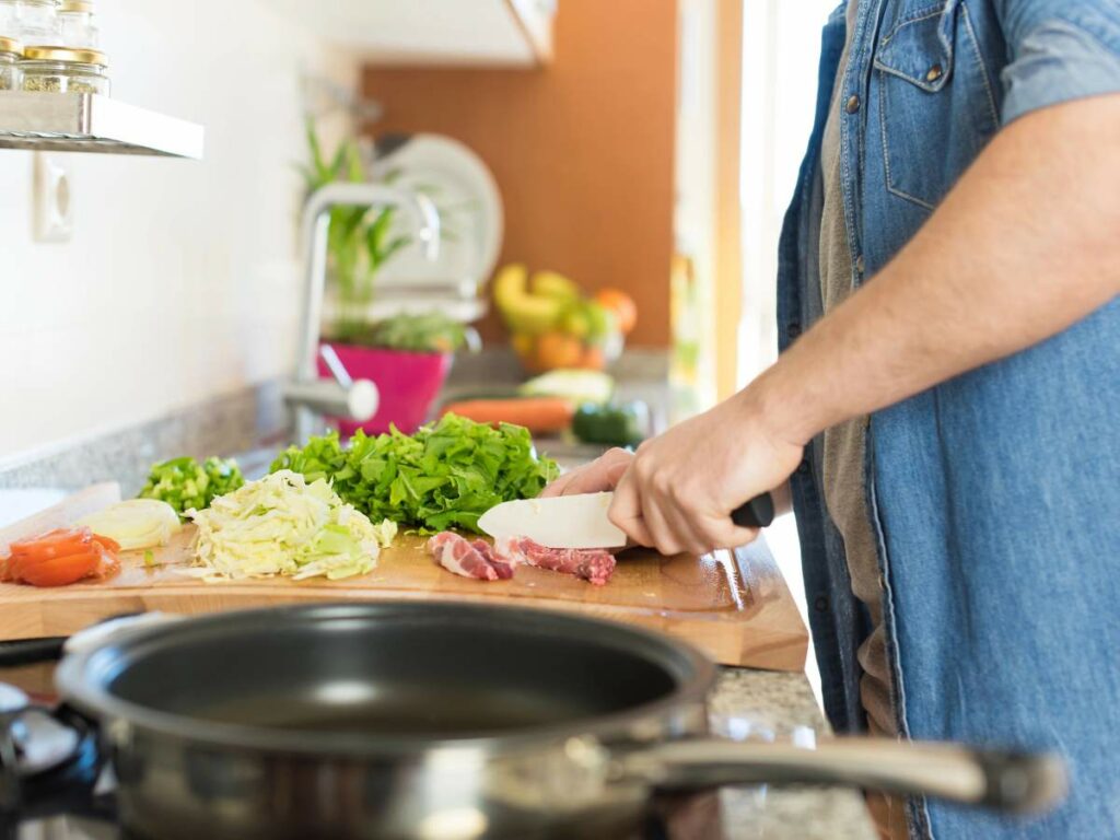 Person chopping vegetables and meat on a wooden cutting.