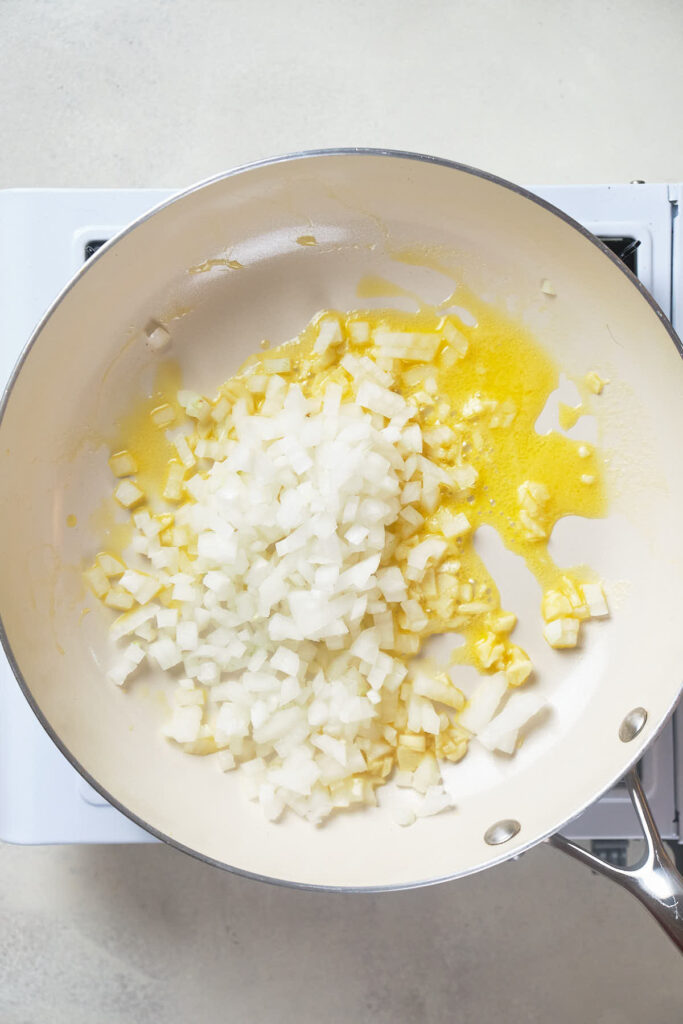 Chopped onions cooking in butter in a pan placed on a stovetop.