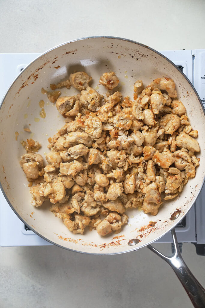 A frying pan filled with browned pieces of cooked chicken sits on a white stove.