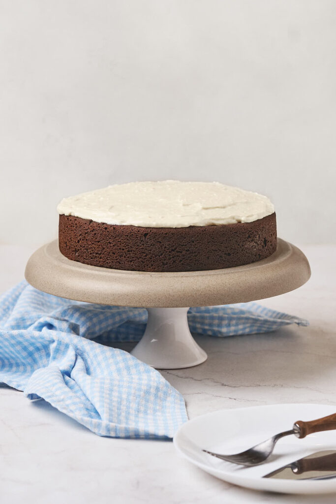 A chocolate cake with white frosting is displayed on a cake stand.