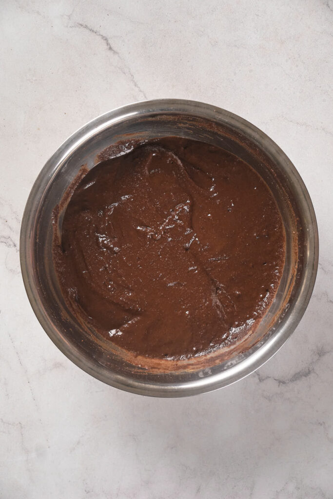 A stainless steel bowl filled with chocolate batter sits on a light-colored countertop.