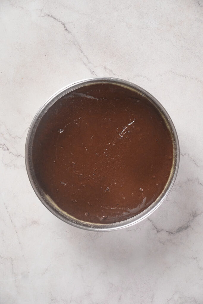 A round metal container filled with a smooth, dark brown liquid, placed on a light gray marble surface.