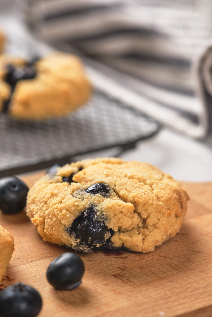 A blueberry scone with whole blueberries on a wooden surface.