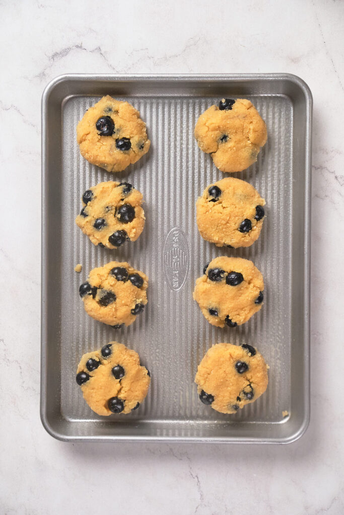 Eight unbaked blueberry scones are arranged on a metal baking tray placed on a marble countertop.