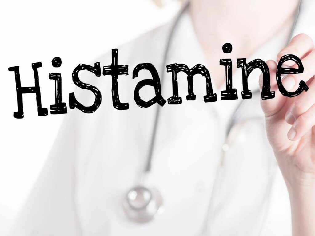 Person in white lab coat and stethoscope writing the word "Histamine" in large, stylized letters.