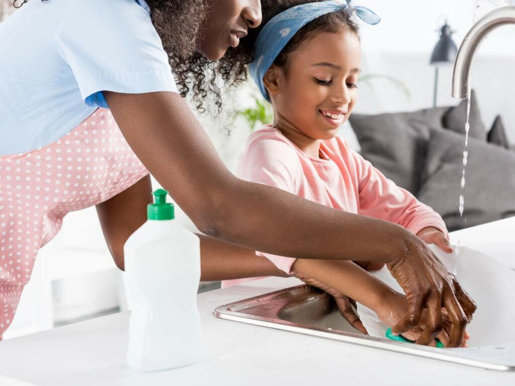 An adult and a child are washing dishes together at a sink.