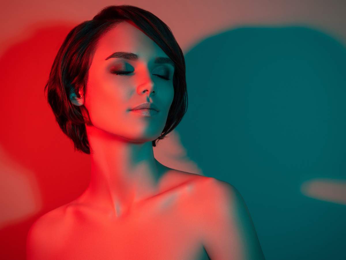 A woman with short hair poses with her eyes closed, bathed in red and blue lighting.