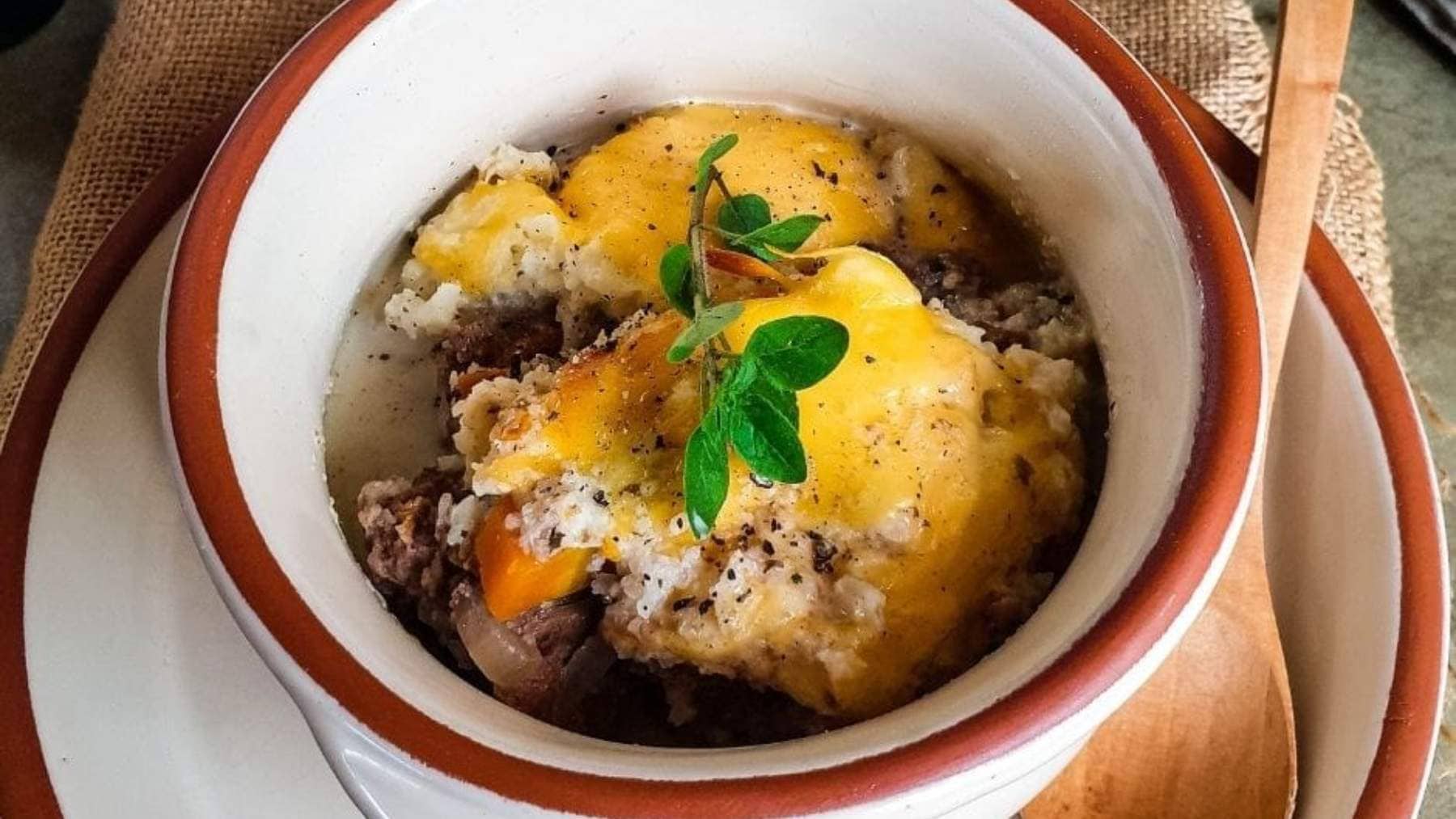 Crockpot Shepherd's Pie in ceramic bowl on matching plate with wooden spoon and oregano garnish.