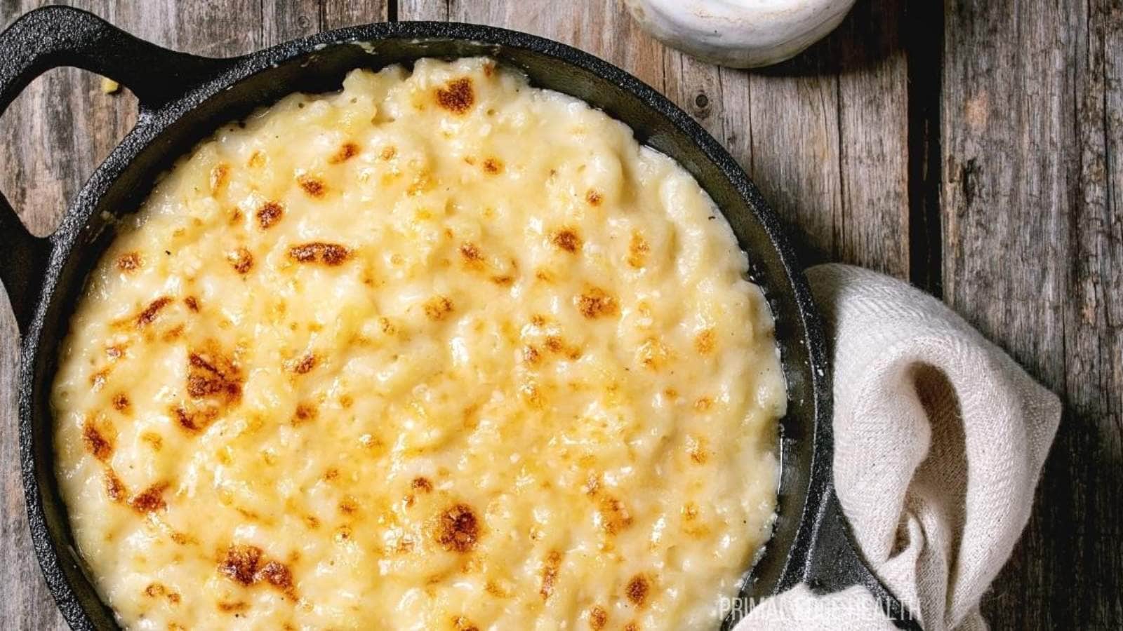 A cast iron skillet filled with baked macaroni and cheese rests on a wooden surface, next to a white napkin.