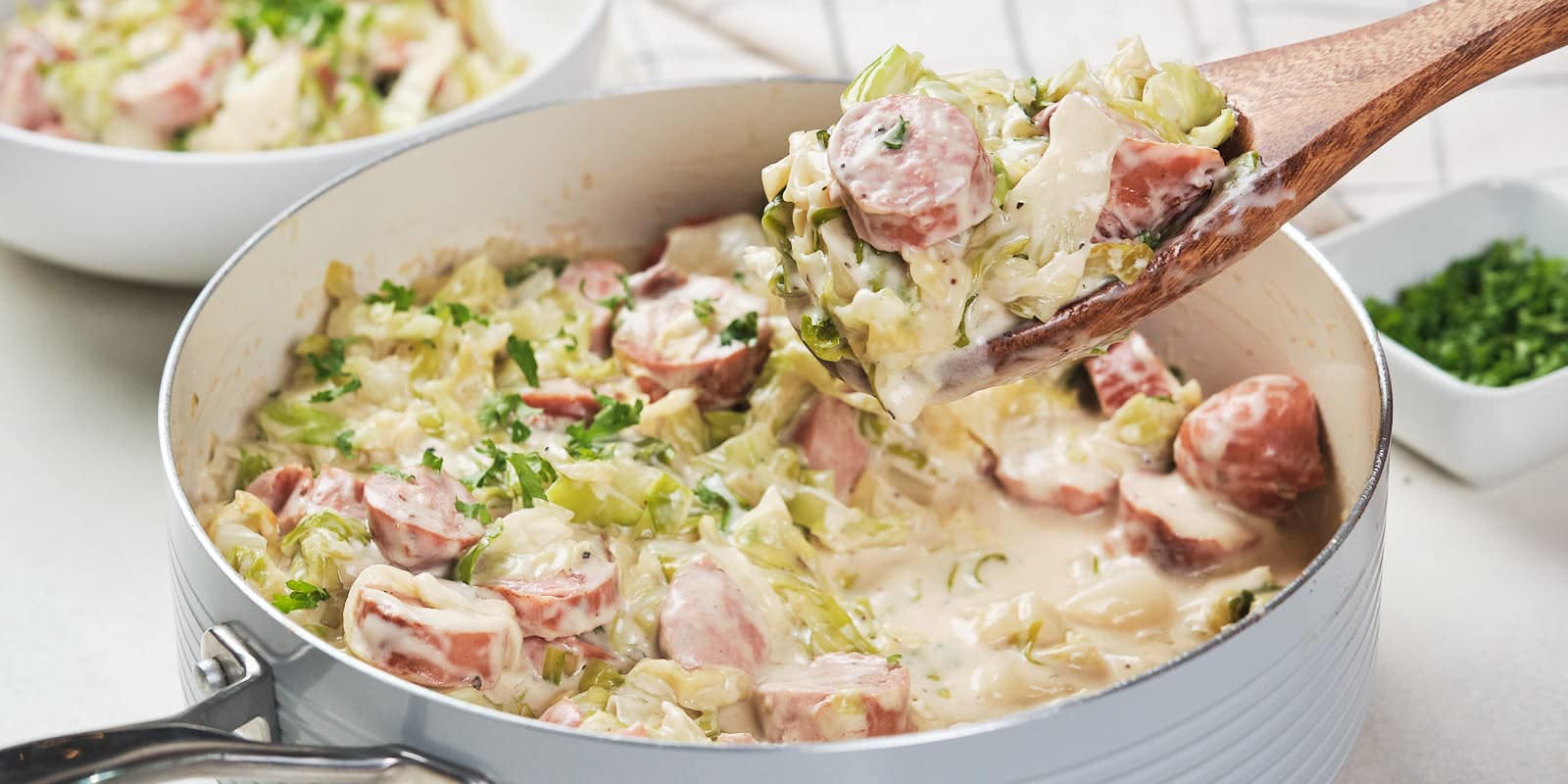 A skillet containing a creamy cabbage and sausage alfredo garnished with herbs.