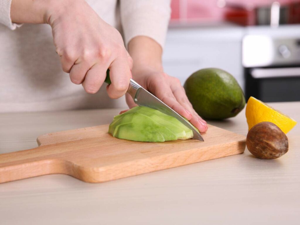 Person slicing an avocado on a wooden cutting board.