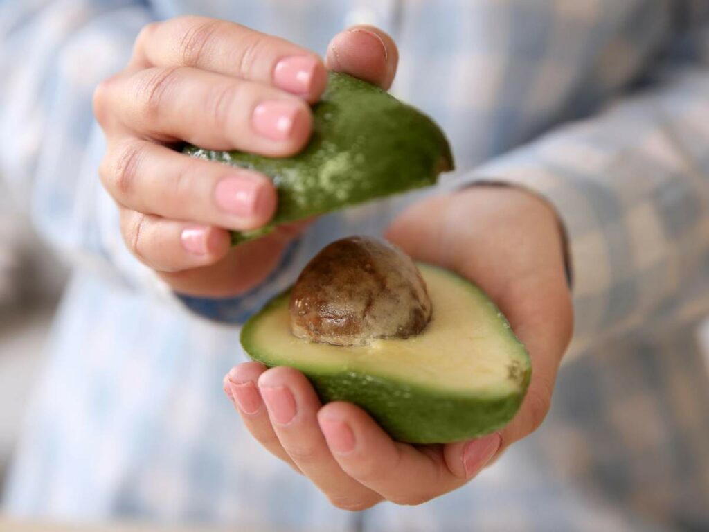 A person holding an avocado, with one half exposing the pit.