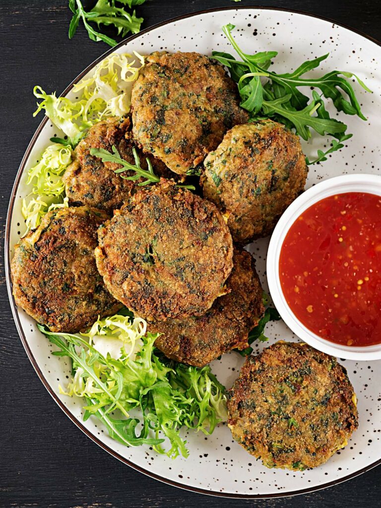 A plate of vegetable patties garnished with leafy greens, served with a small bowl of red dipping sauce.