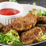 A plate of falafel with a side of fresh greens and a small bowl of red dipping sauce.