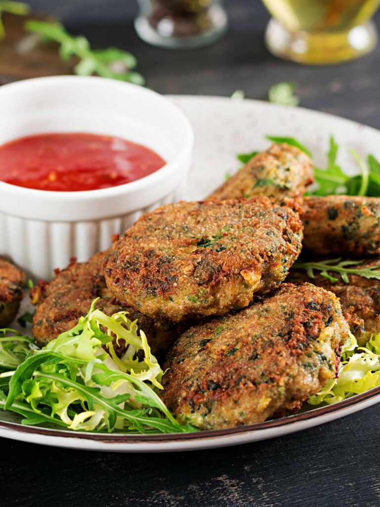 A plate of falafel with a side of fresh greens and a small bowl of red dipping sauce.