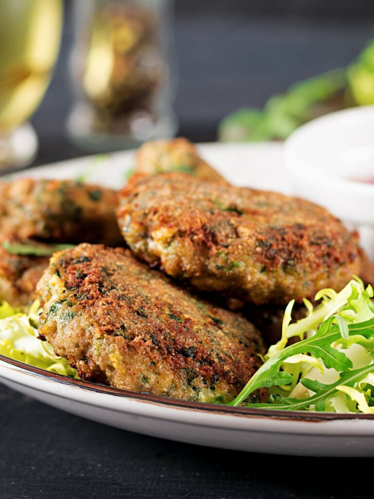Plate of three pan-fried vegetable patties placed on a bed of shredded greens.