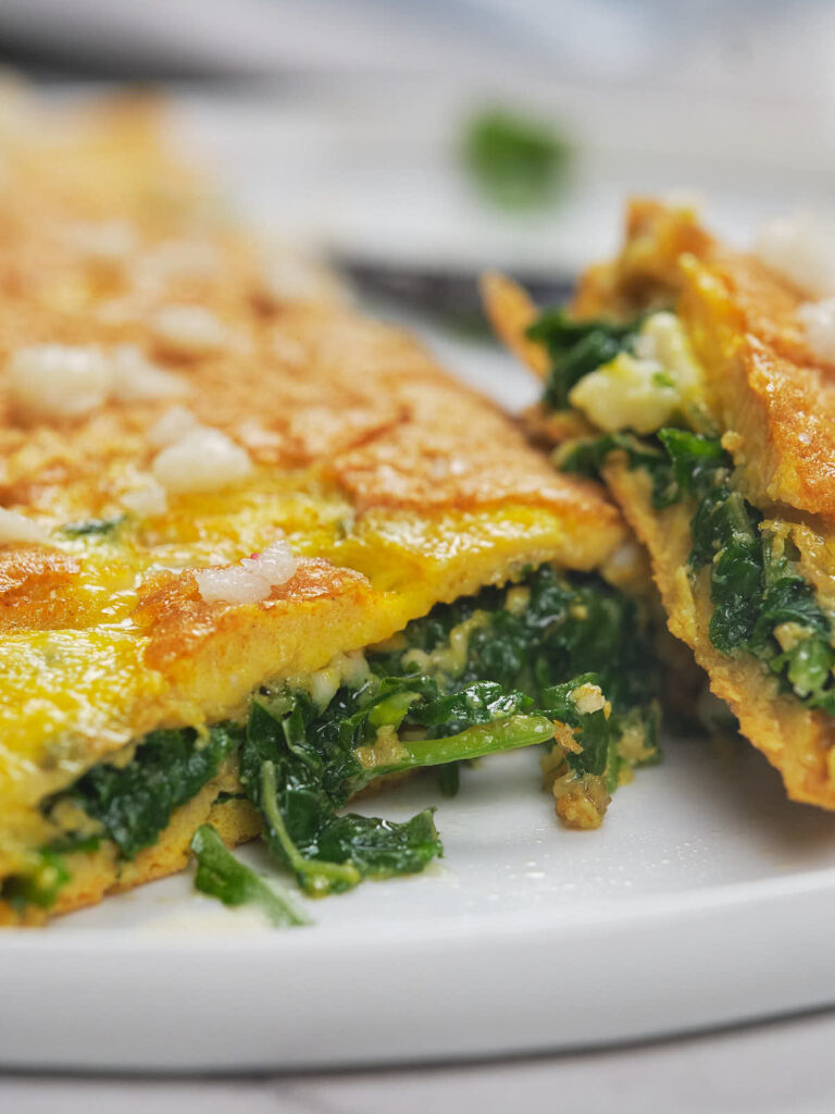 A close-up of a folded omelette filled with cooked spinach on a white plate.
