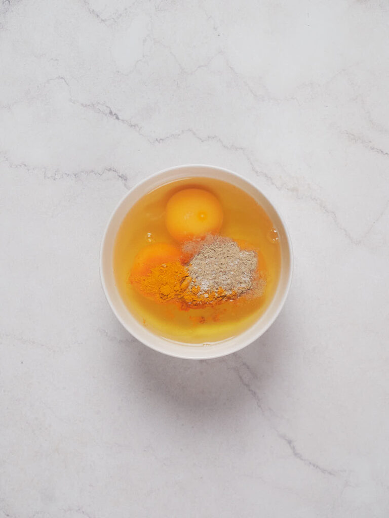 A white bowl containing two cracked eggs, yellow yolks visible, atop a grayish marble surface.