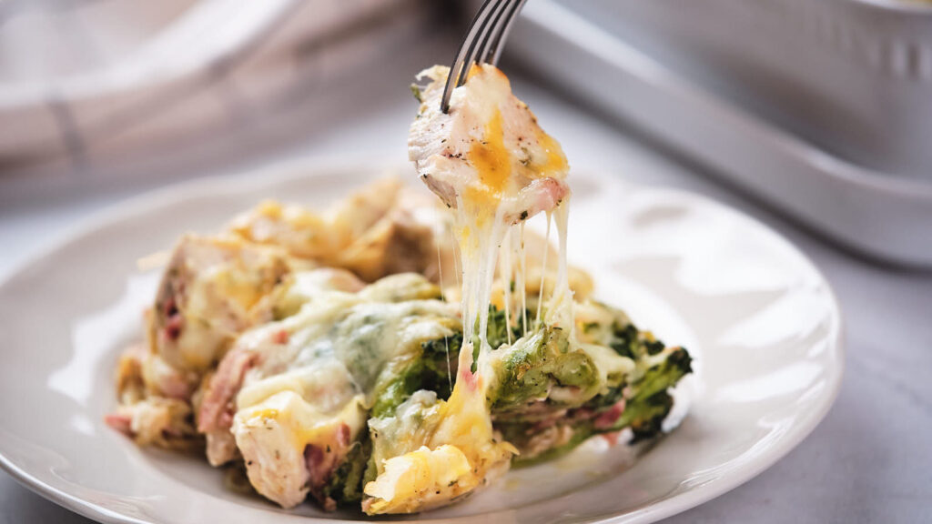 A fork lifting a portion of chicken bacon ranch casserole from a white plate.