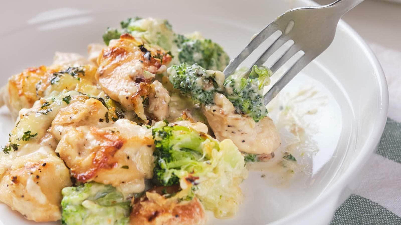 A fork with a piece of chicken broccoli Alfredo casserole on a white plate.