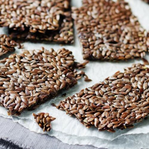 Crackers made of flax seeds are arranged on a piece of white parchment paper.