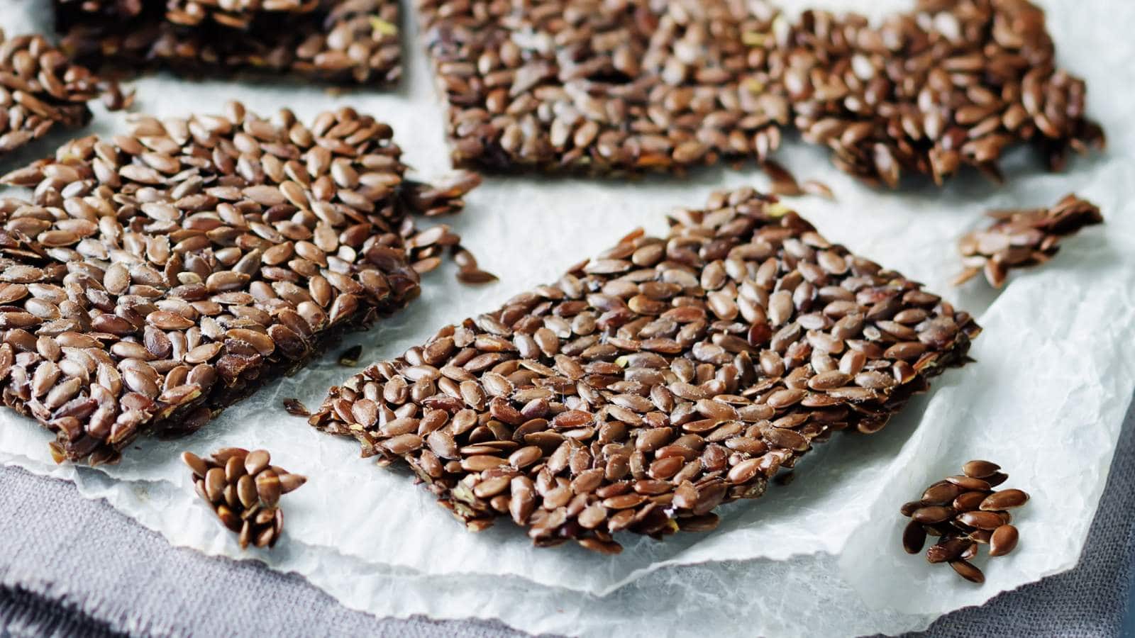 Rectangular flaxseed crackers are arranged on a crumpled sheet of parchment paper with some seeds scattered around.