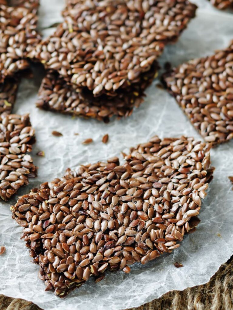 Several pieces of flaxseed crackers are displayed on a piece of parchment paper.
