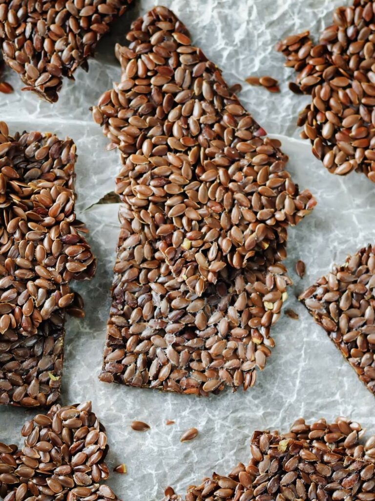 Close-up of flaxseed crackers broken into irregular pieces on a parchment paper background.