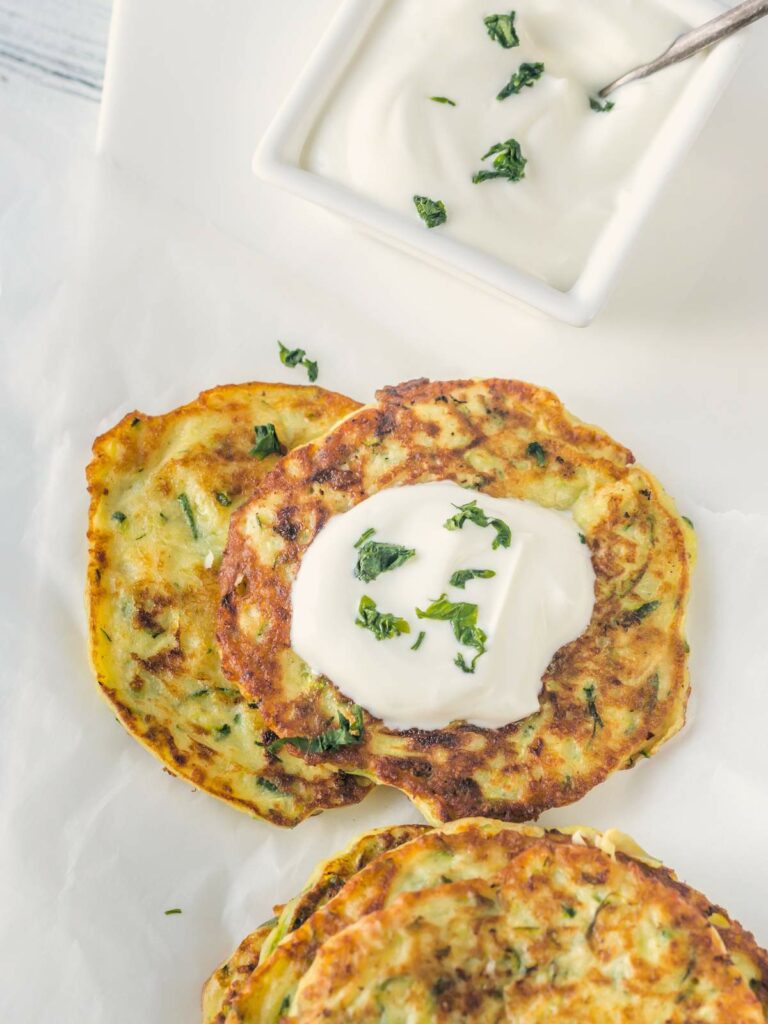 Three zucchini fritters with a dollop of sour cream and chopped herbs on top.