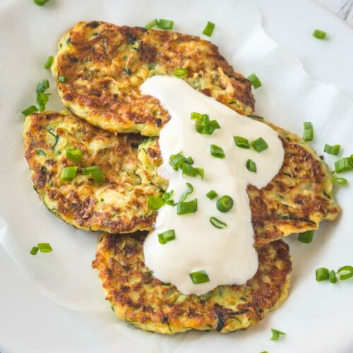 Close-up of three zucchini fritters topped with a dollop of sour cream and garnish.