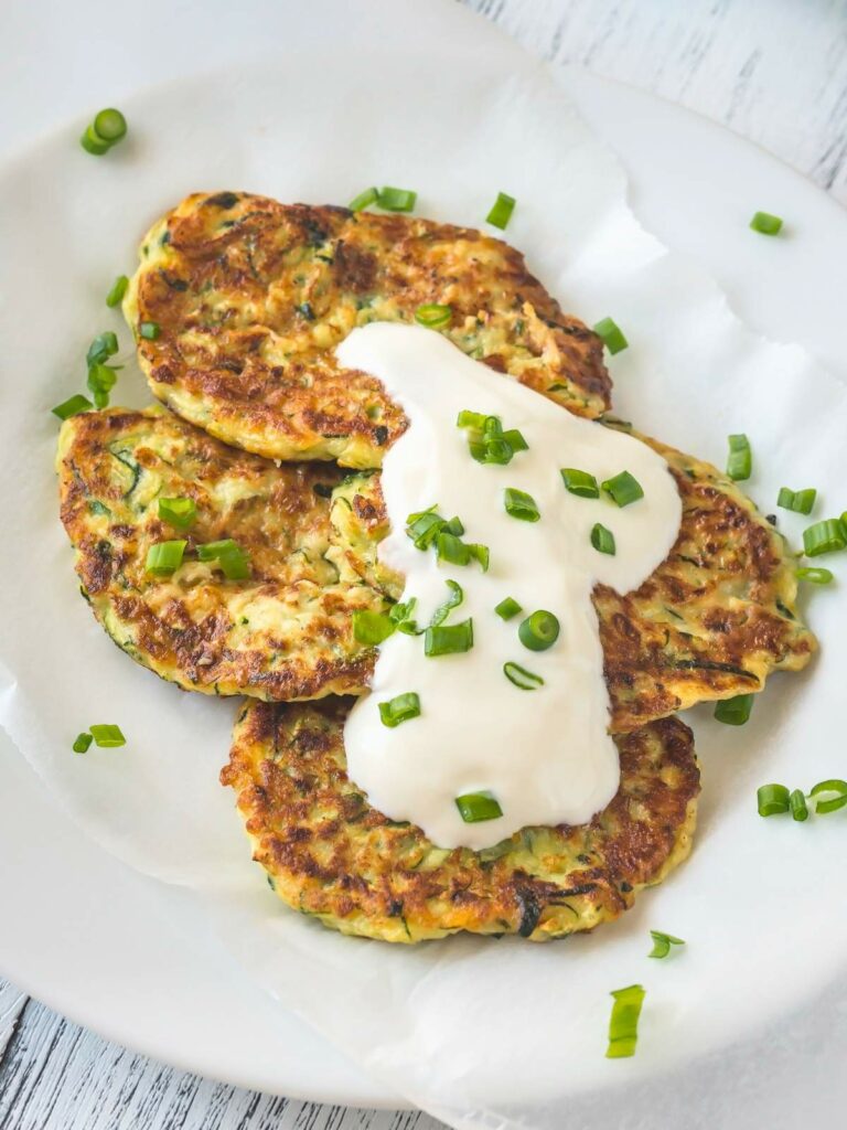 Close-up of three zucchini fritters topped with a dollop of sour cream and garnish.
