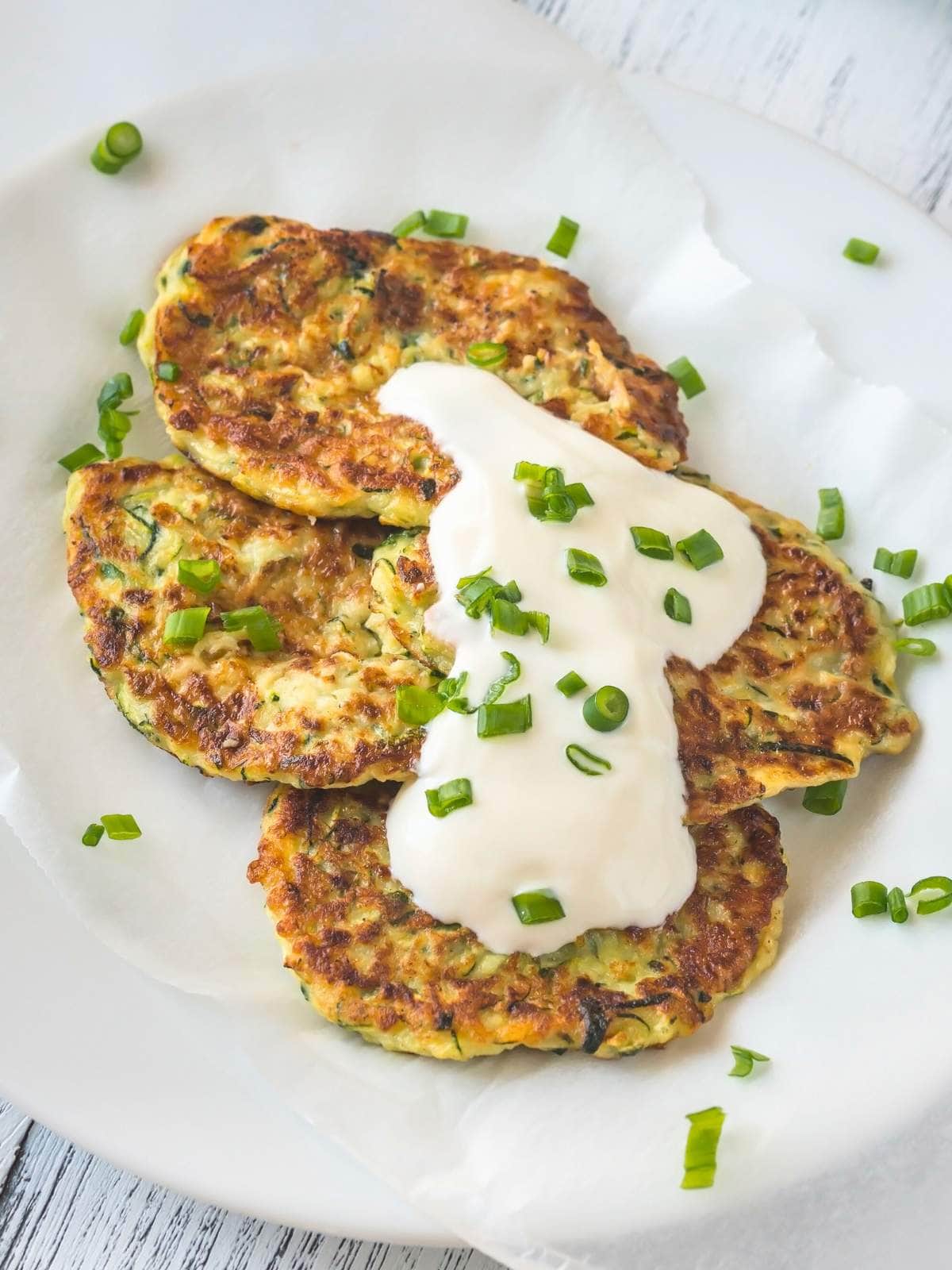 Close-up of three zucchini fritters topped with a dollop of sour cream and garnish.