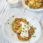 Plate of zucchini fritters topped with sour cream and chopped chives.