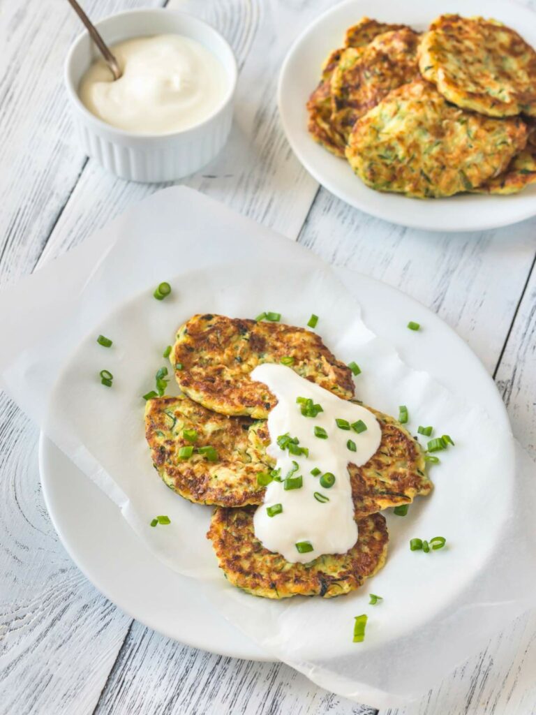 Plate of zucchini fritters topped with sour cream and chopped chives.