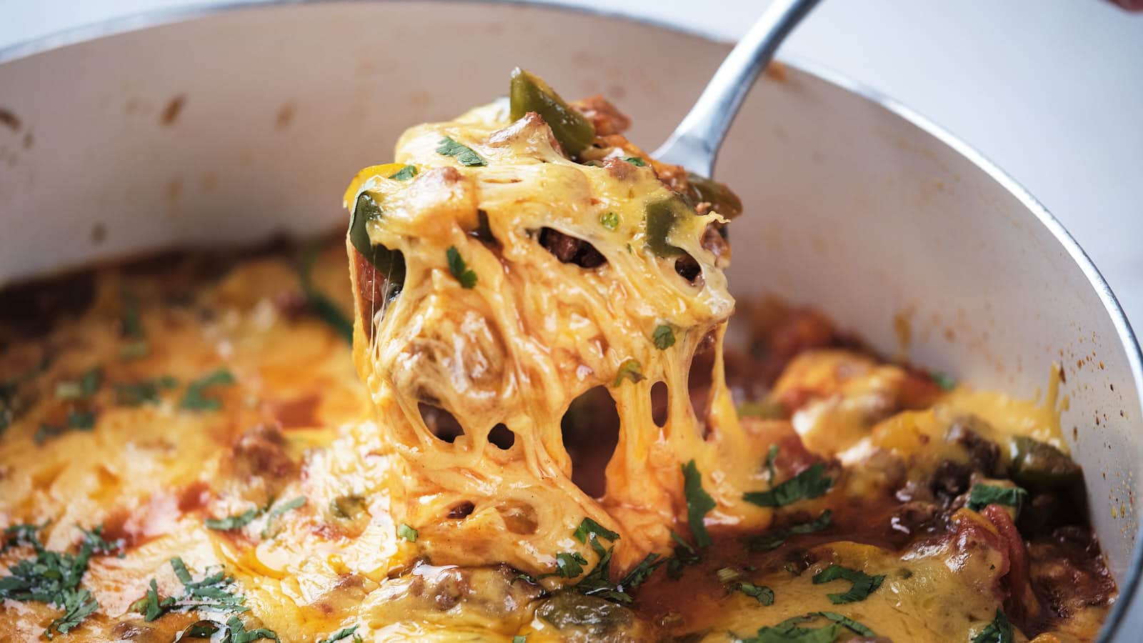 A skillet with a cheesy ground beef and vegetable casserole, sprinkled with herbs, displayed on a table.