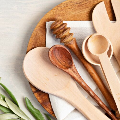 A wooden plate holds various wooden kitchen utensils, including spoons, a honey dipper, and a fork.