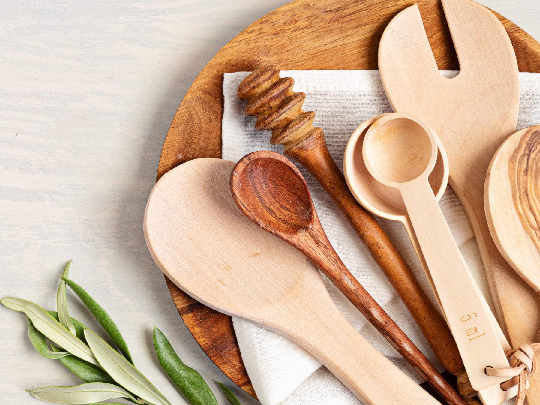 A wooden plate holds various wooden kitchen utensils, including spoons, a honey dipper, and a fork.