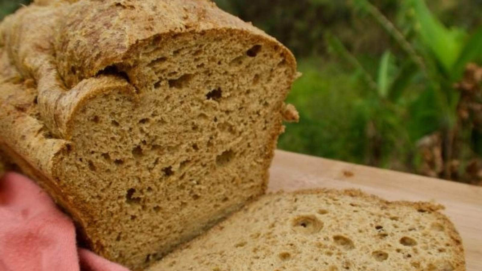 A close-up of a loaf of bread with a slice cut off, placed on a wooden surface.