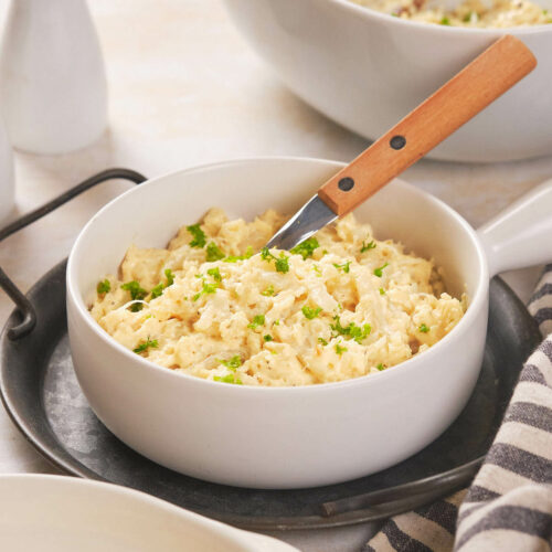 A white bowl filled with scrambled cauliflower garnished with chopped herbs.