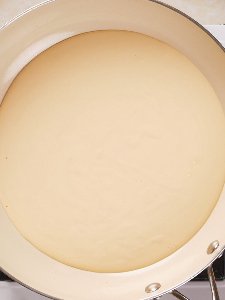 A close-up view of a creamy beige liquid in a white frying pan.