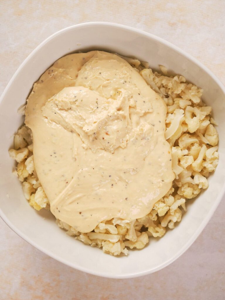 A white bowl filled with chopped cauliflower topped with a thick, creamy sauce.