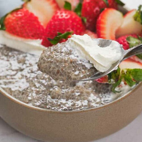 A bowl of chia pudding topped with sliced strawberries and a dollop of whipped cream.
