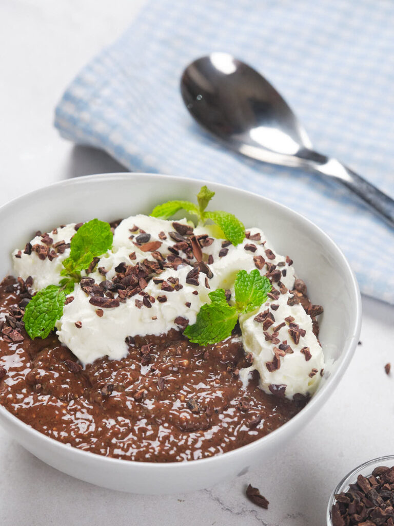 A bowl of chocolate chia pudding next to a spoon on a checkered cloth.