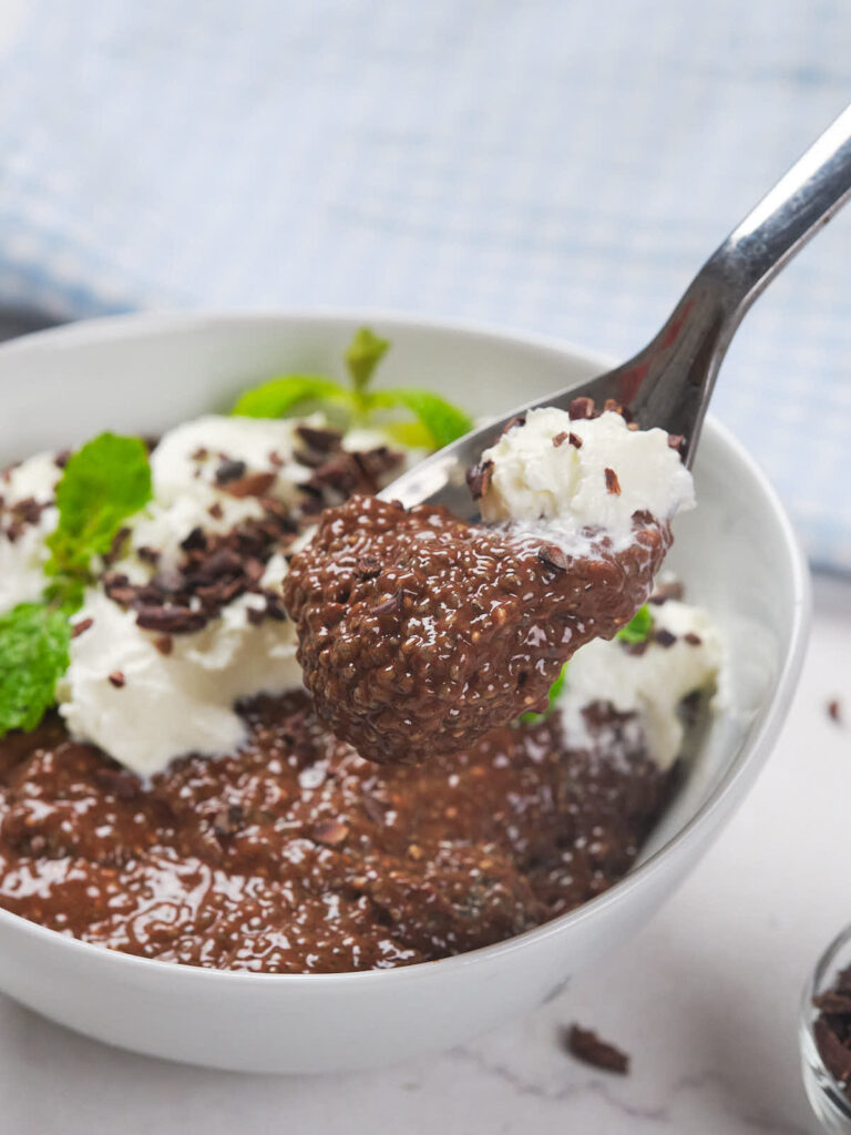 A bowl of chocolate chia pudding topped with whipped cream, mint leaves, and chocolate shavings.