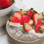 A bowl of chia seed pudding topped with whipped cream and sliced strawberries.