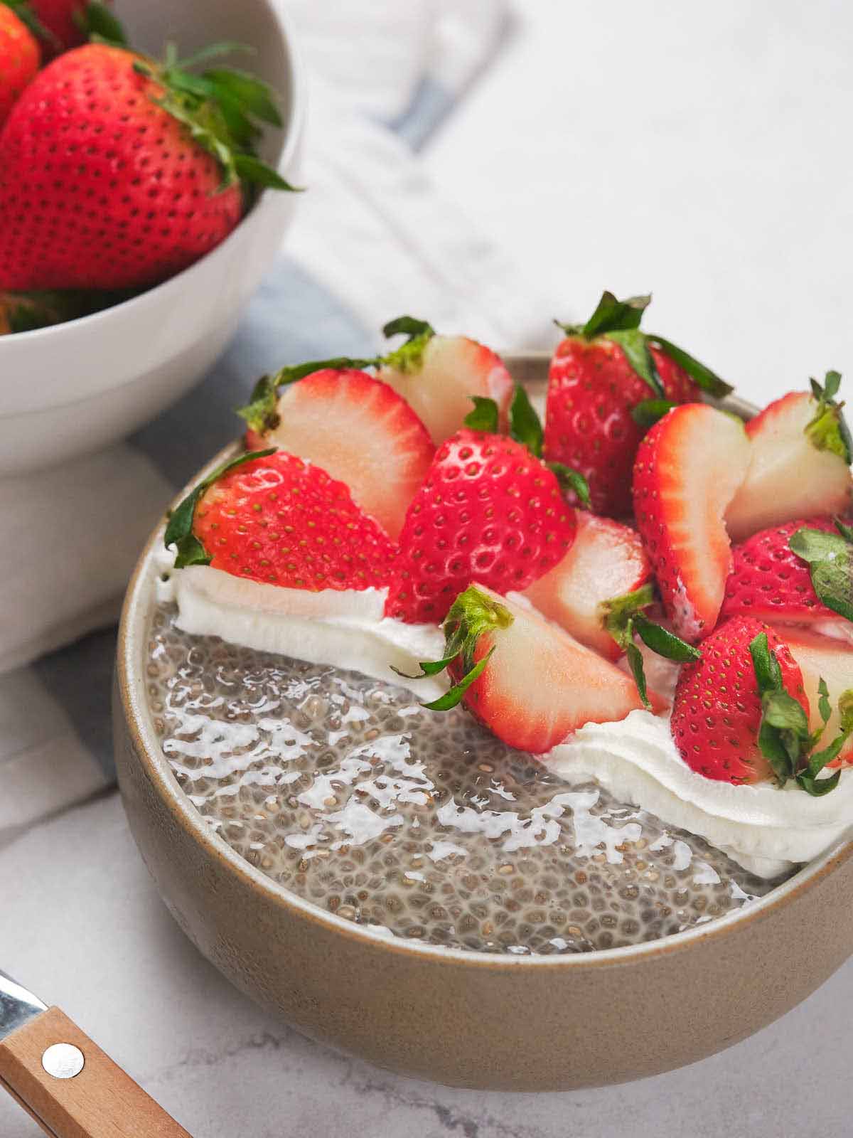 A bowl of chia seed pudding topped with whipped cream and sliced strawberries.